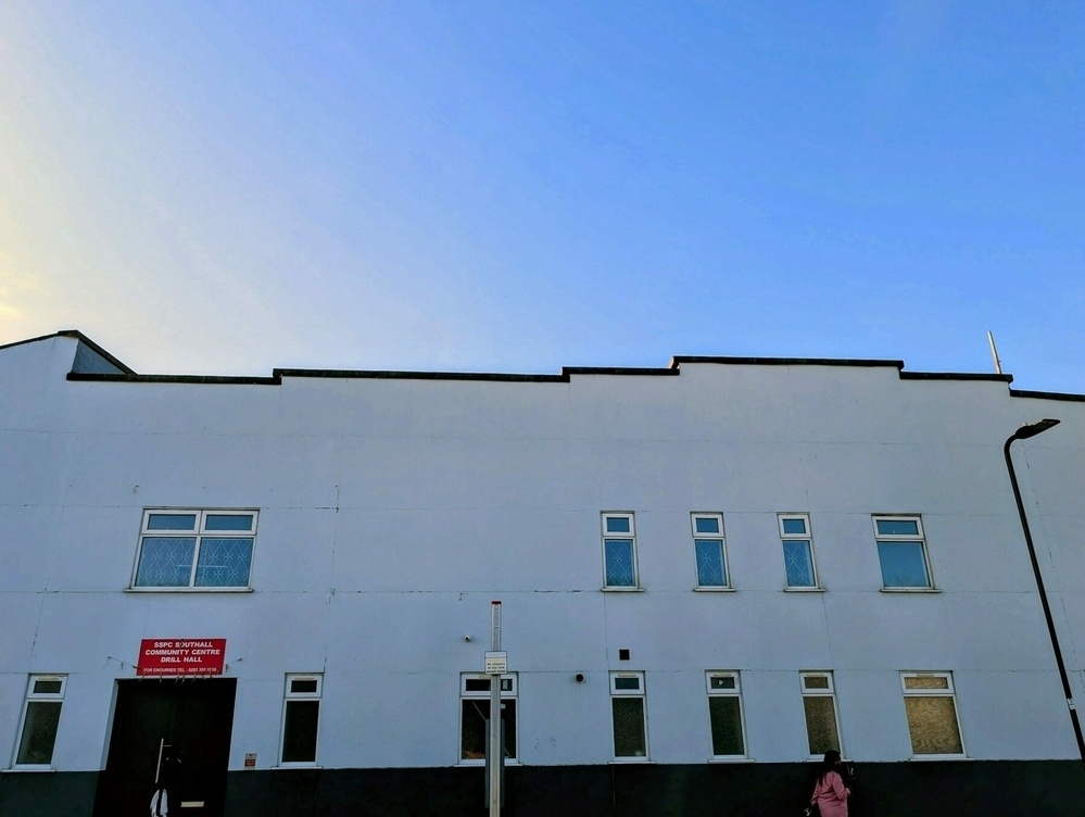 A white building with multiple windows and a red sign stands against a clear blue sky.