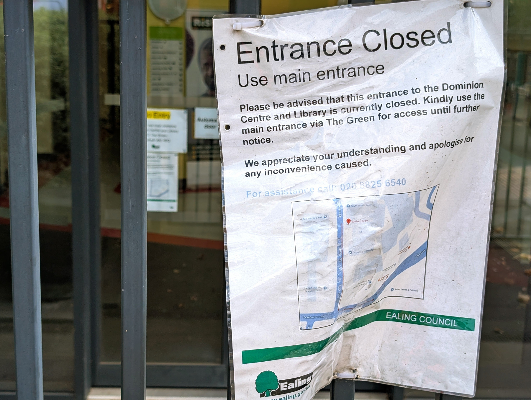 Weathered notice inside a plastic sleeve tied to bolted black iron gates informs visitors that the rear entrance to the new library building is closed.