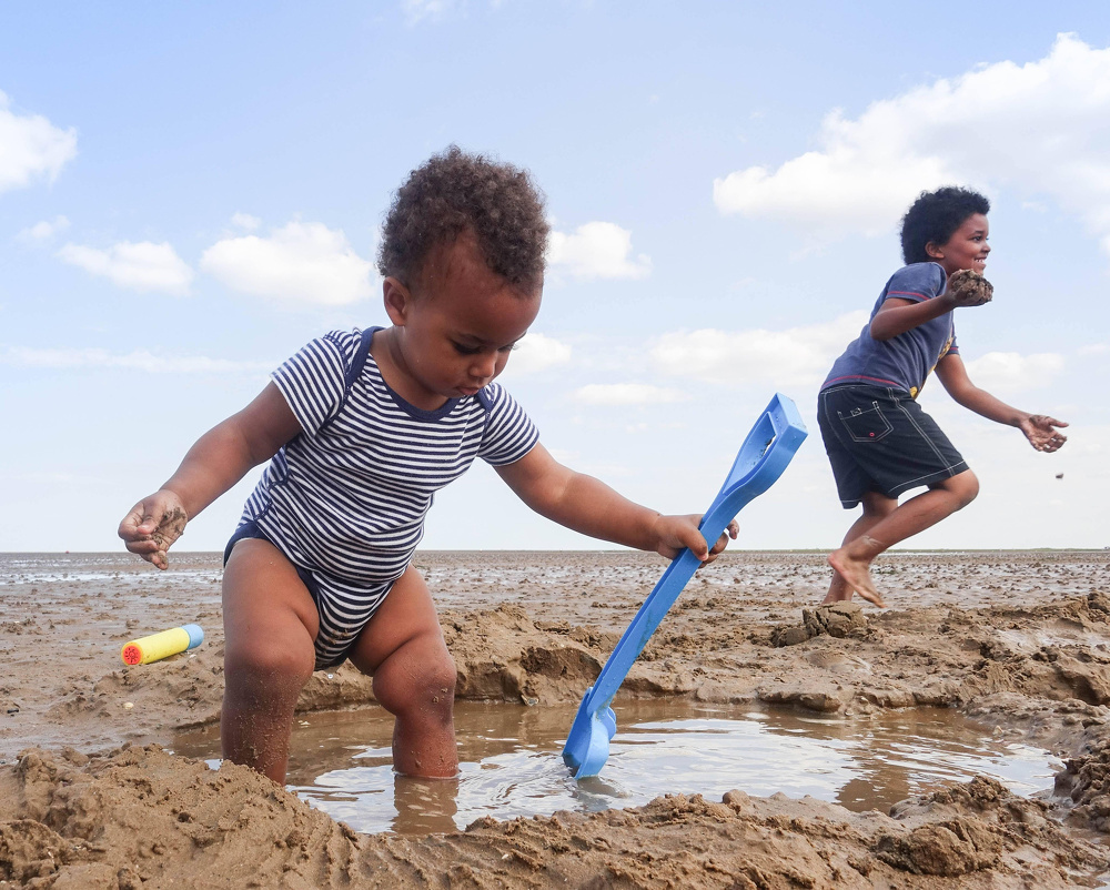 Two children are playing and digging in the sand at the beach on a sunny day.