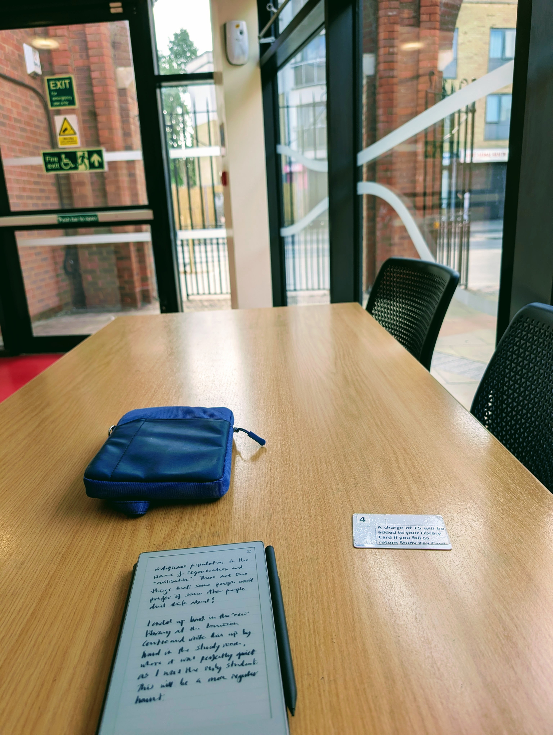 Inside the new library study room, my notebook, case and keycard sit on a conference desk surrounded by chairs looking out on to the high street through glass panelled walls.
