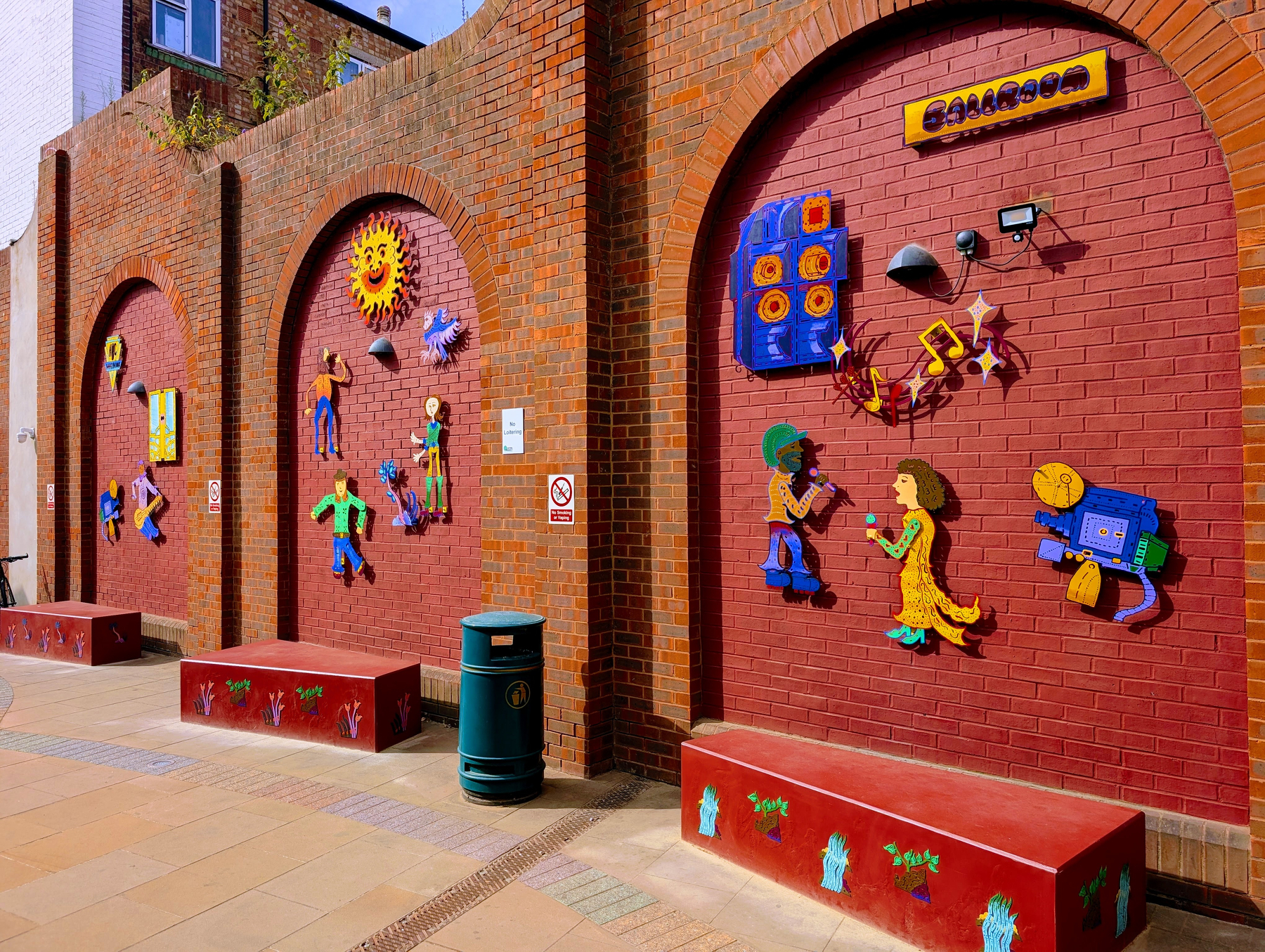 The wall outside the new library building hosts a colourful mosaic depicting the site's heritage as a cinema and dance hall with a sign warning NO LOITERING.