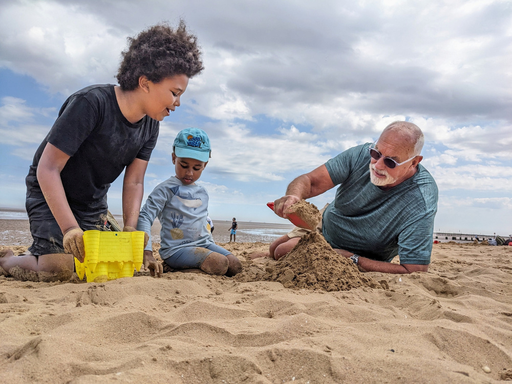 A man and two children are playing together, building a sandcastle on a beach.