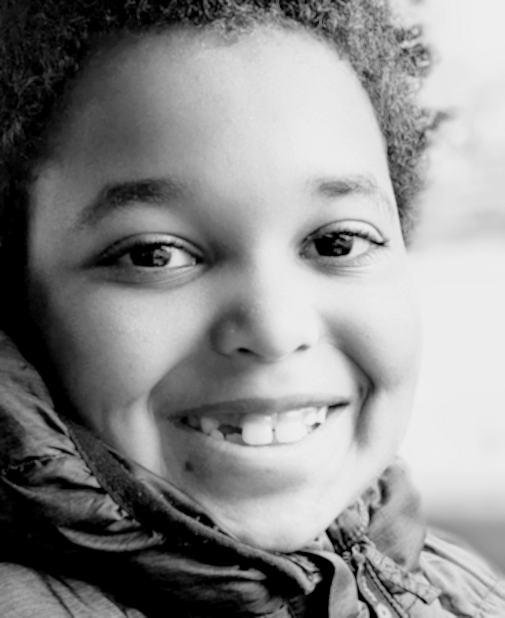 A smiling child with curly hair is wearing a jacket and looking directly at the camera.