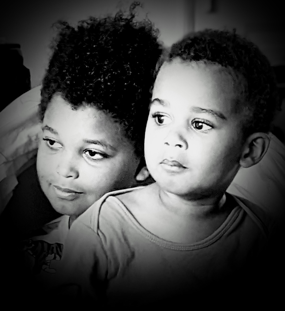 Two children are closely positioned together, looking intently in the same direction with calm expressions.