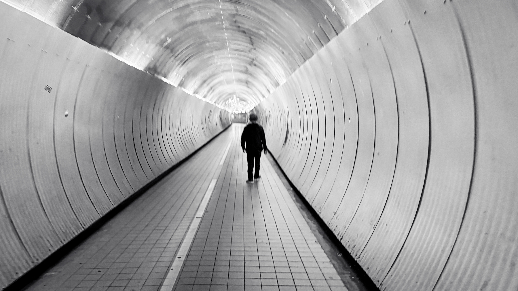 En person går ensam genom en lång, tom och rund tunnel med metallväggar.