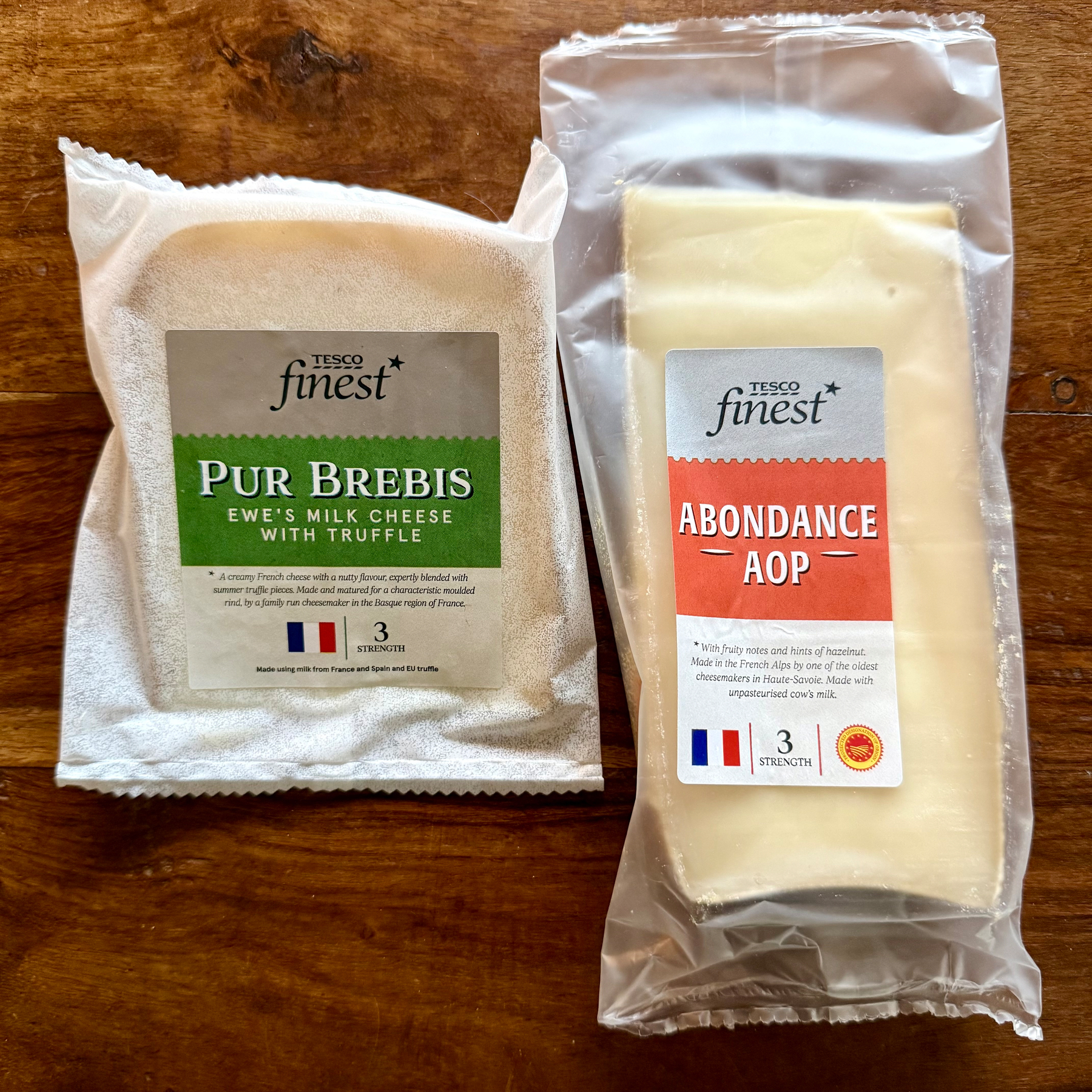 Two packages of Tesco Finest French cheese are displayed on a wooden surface, one labeled Pur Brebis (ewe's milk cheese with truffle) and the other Abondance AOP.